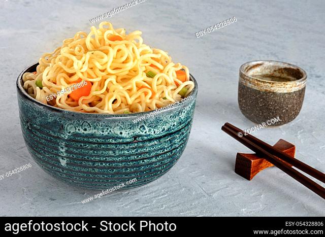 Instant noodles bowl with carrot and scallions, with chopsticks and sake