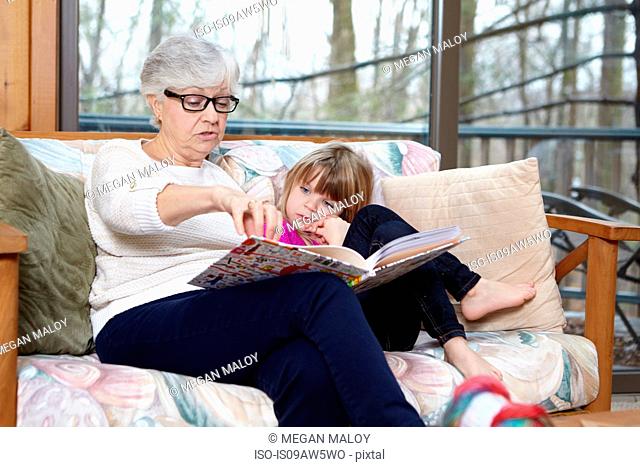 Senior woman reading story to granddaughter on living room sofa
