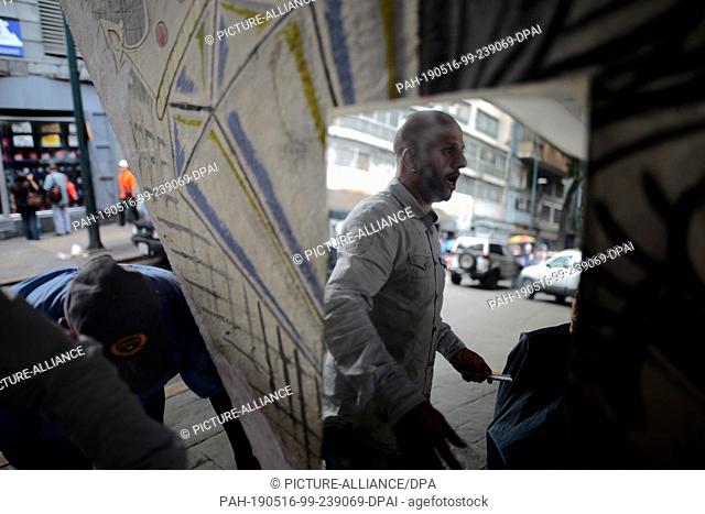 13 May 2019, Venezuela, Caracas: Jose Joserondon, hairdresser, talks about the current political situation while cutting the hair of a customer on the street