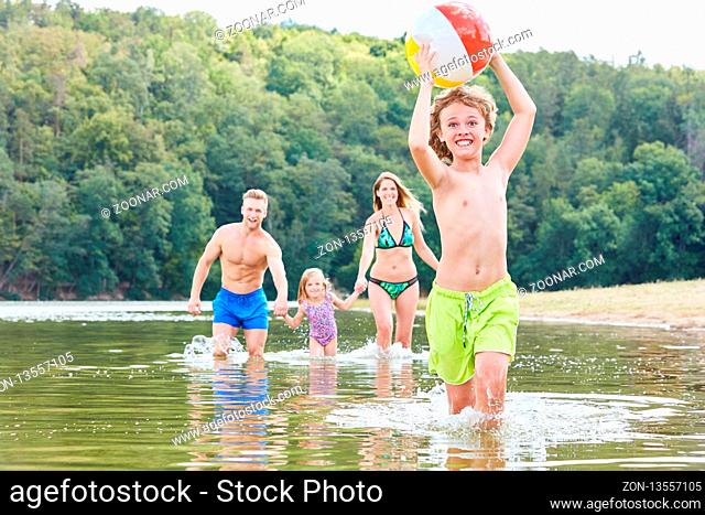 Junge läuft mit einem Ball durchs Wasser beim Spielen mit seiner Familie im Meer