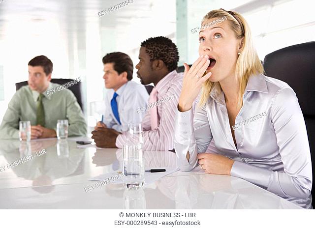 Four businesspeople in boardroom with one businesswoman yawning