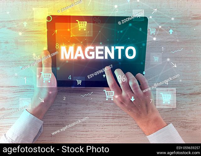 Close-up of a hand holding tablet with MAGENTO inscription, online shopping concept
