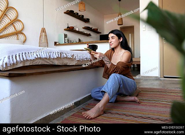 Young woman enjoying coffee and using phone at home