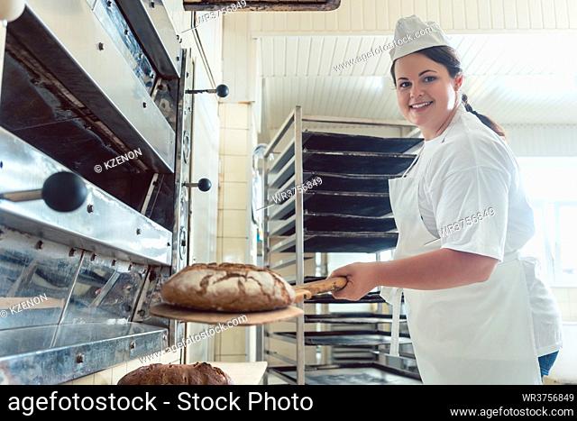 Smiling baker getting fresh bread with shovel out of oven