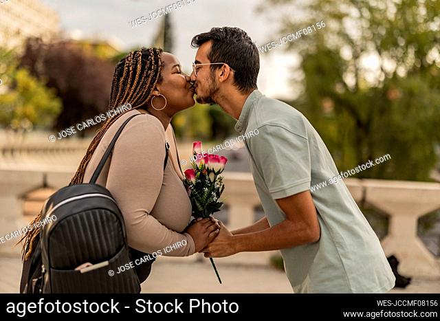 Young couple kissing each other with bouquet of flowers at footpath