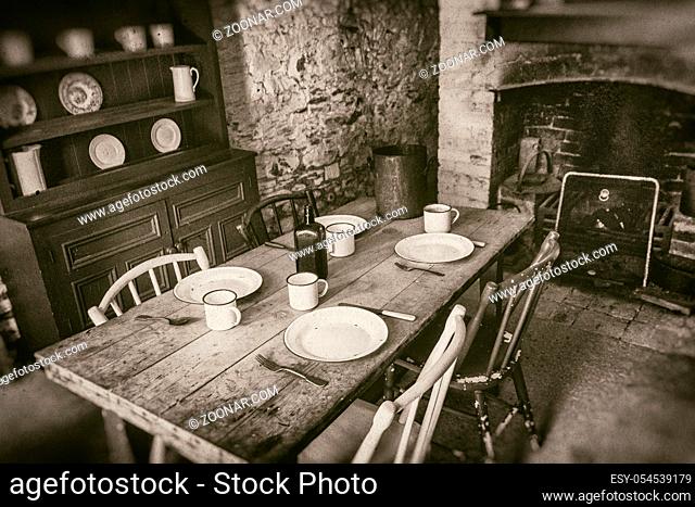 Poor peasants interior from 19th century, dining room with set wooden table and fireplace, sepia style photography