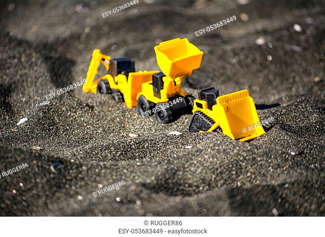 Toy construction machinery in black sand. Yellow and black colors toy machines. Bulldozer, loader, excavator