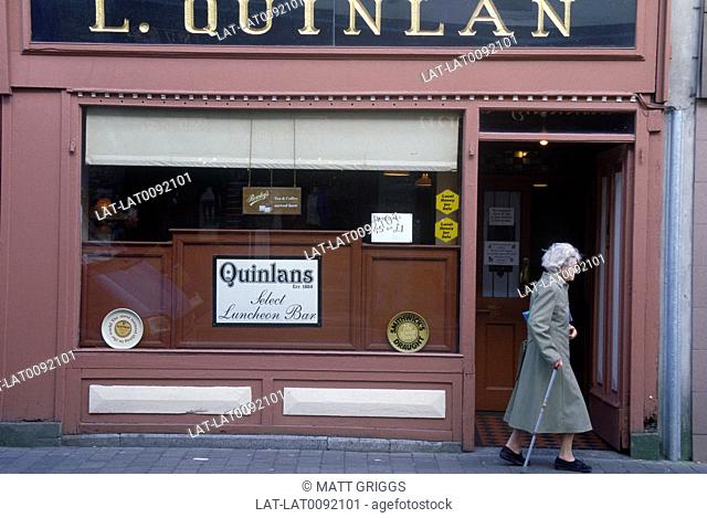 Quinlan's Bar. Sign. Facade. Elderly woman with walking stick passing door