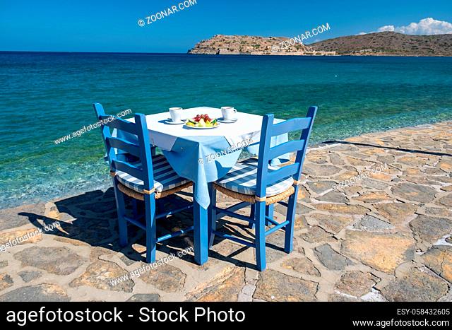 Crete Greece Plaka Lassithi with is traditional blue table and chairs and the beach in Crete Greece. Paralia Plakas, Plaka village Crete. Europe