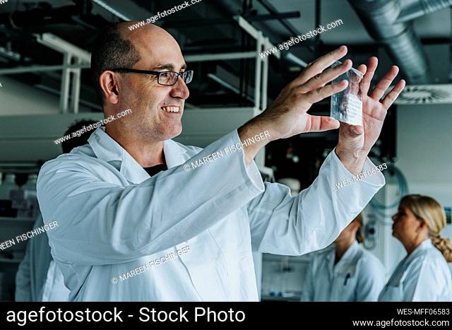 Scientist smiling while examining human brain slide with coworker standing in background at laboratory