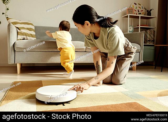 Mother turning on robotic vacuum cleaner looking at daughter at home
