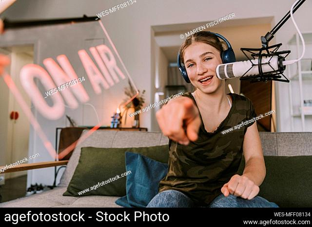 Smiling teenage girl pointing while broadcasting at home