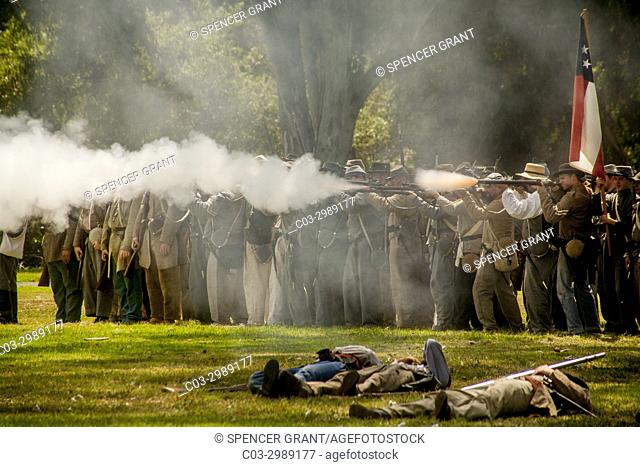 Rifle-carrying ""Confederate"" soldiers fire a volley at a Civil War battle reenactment in a Huntington Beach, CA, park. Note ""wounded"" soldiers in foreground
