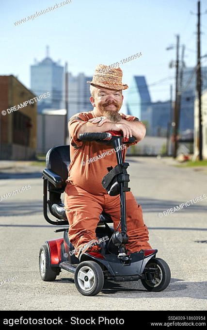 Portrait of male dwarf in sitting on scooter, looking into camera with big smile