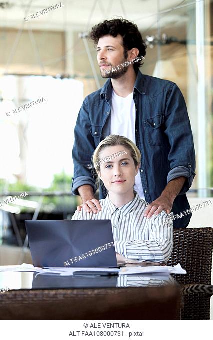 Man massaging woman's shoulders as she works on laptop computer