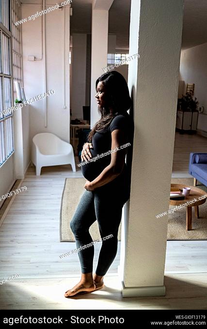 Pregnant woman leaning against column at home