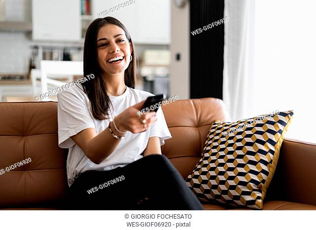 Happy young woman sitting on couch at home watching Tv