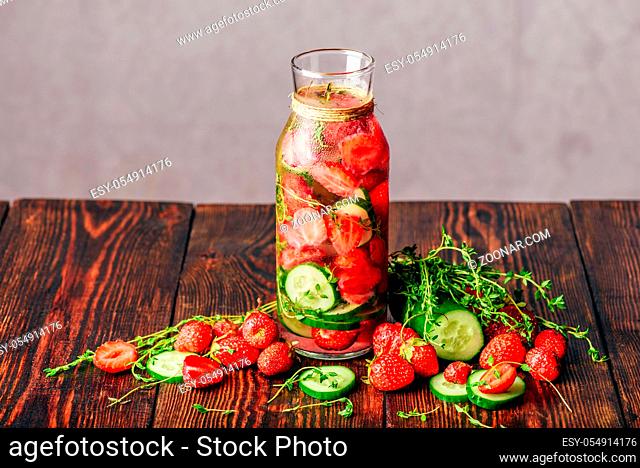 Bottle of Infused Water with Fresh Strawberry, Sliced Cucumber and Springs of Thyme. Ingredients Scattered on Wooden Table. Copy Space