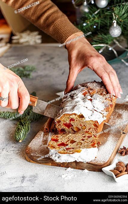 Stollen is fruit bread of nuts, spices, dried or candied fruit, coated with powdered sugar. Close up hands of the chef slicing a cake with a knife at pastry...