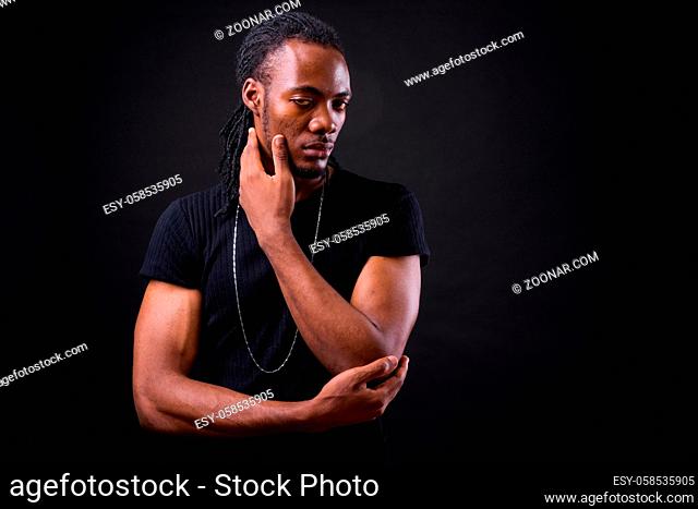 Studio shot of young handsome African man with dreadlocks against black background
