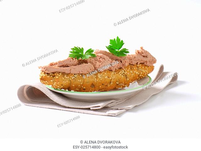 fresh bread roll with pate and parsley on white plate and place mat