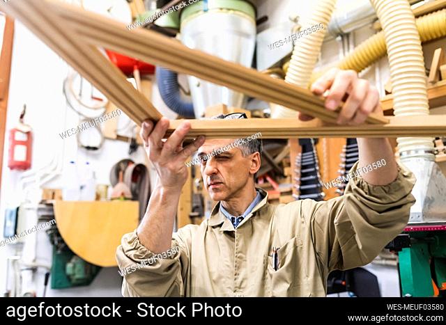 Concentrated male craftsperson looking at triangular wood in workshop