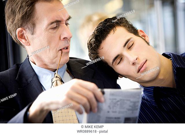 Close-up of a young man asleep on a mature mans shoulder