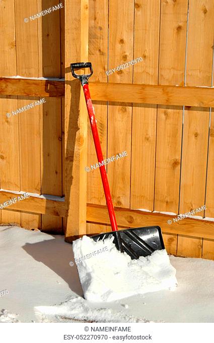 Wooden fence holds up a snow shovel. Shovel has snow on it