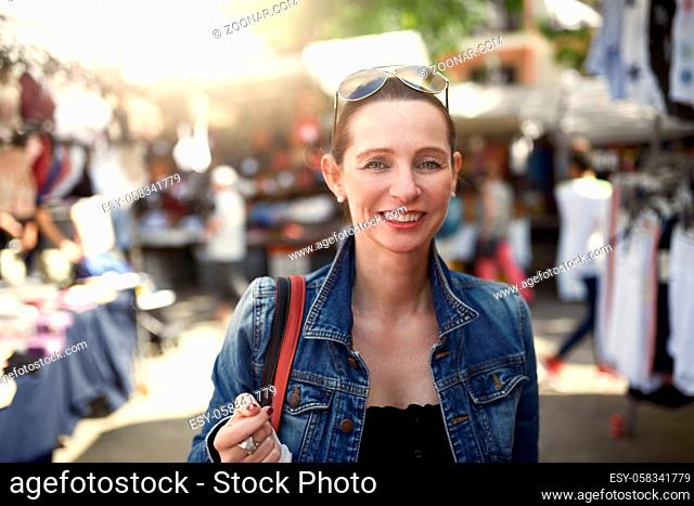 Happy attractive stylish woman shopping at an outdoor market standing looking at the camera with a wide warm friendly smile