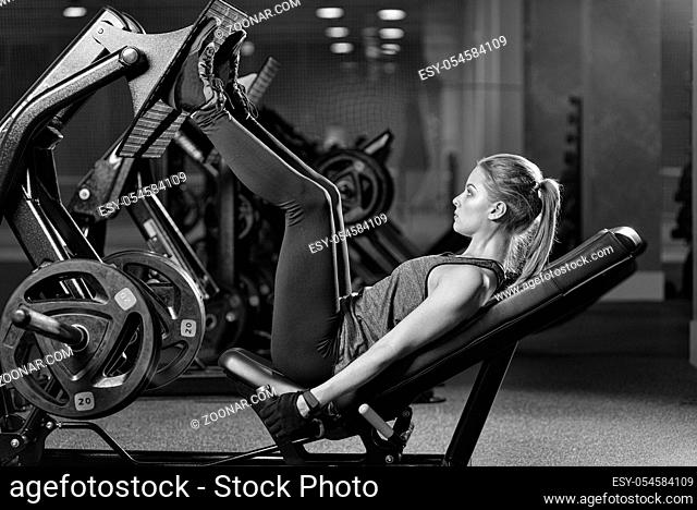 Sportive woman using weights press machine for legs at the gym. Pretty brunette exercising in a simulator. Working her quads at machine