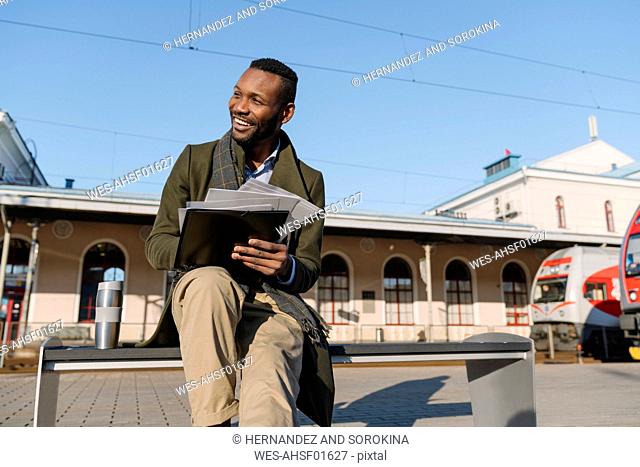 Portrait of happy businessman with documents waiting for the train