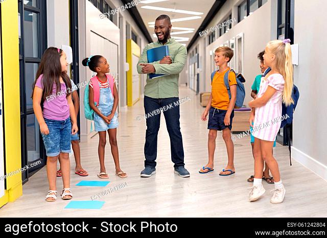 African american young male teacher talking to multiracial elementary students standing in corridor