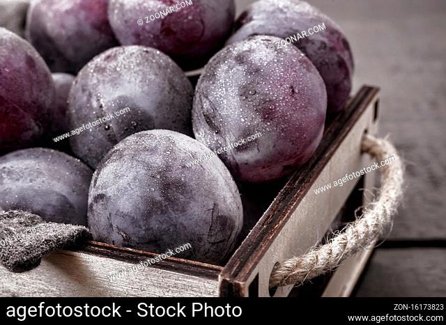 On the table in a drawer are large ripe plums. Presented in close-up on a dark background. The view from the top
