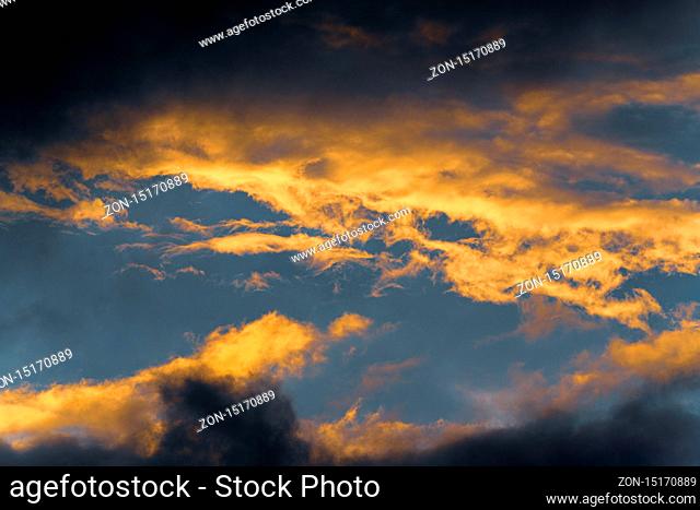 Stunning fluffy thunderstorm clouds illuminated by disappearing rays at sunset and dark thunderclouds floating across sunny blue sky to change season weather