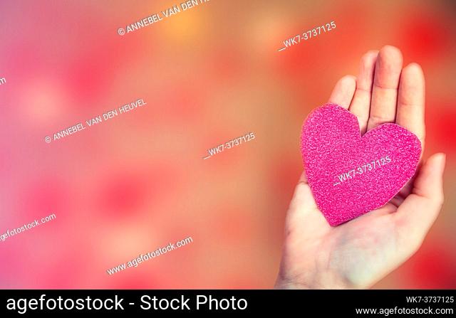 Female hand holding pink glitter heart on romantic blurred bokeh background, copy space or space for text, Valentine's day or romantic background top view