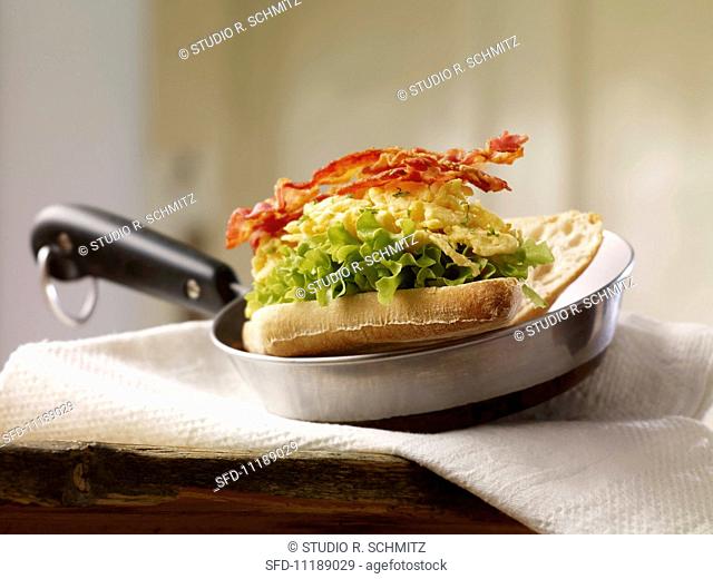 Baguette sandwich filled with scrambled egg, lettuce and crispy bacon