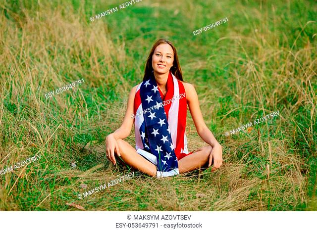 Girl is sitting on the grass with the American flag