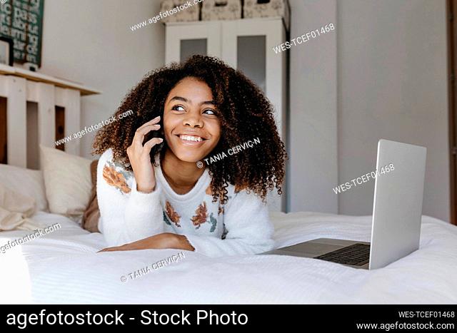 Happy woman talking on mobile phone while resting on bed at home