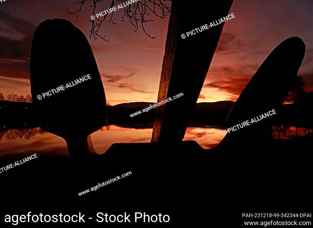 18 December 2023, Saxony-Anhalt, Wernigerode: The silhouette of an anchor appears in the light of the setting sun on a pond near Wernigerode