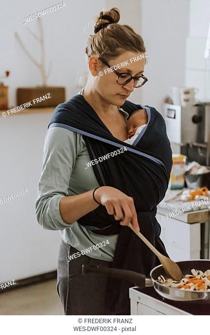 Mother with baby in baby sling cooking