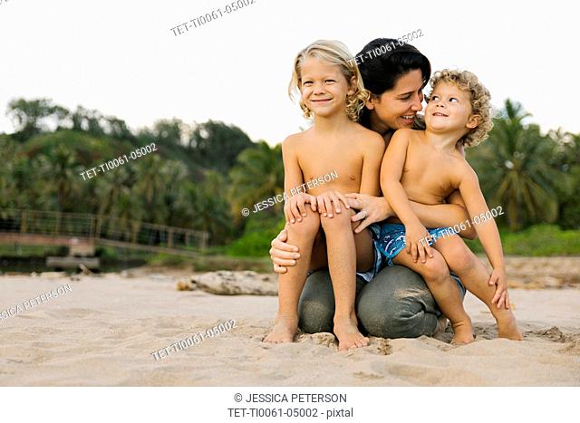 Woman with her sons sitting on her lap on beach