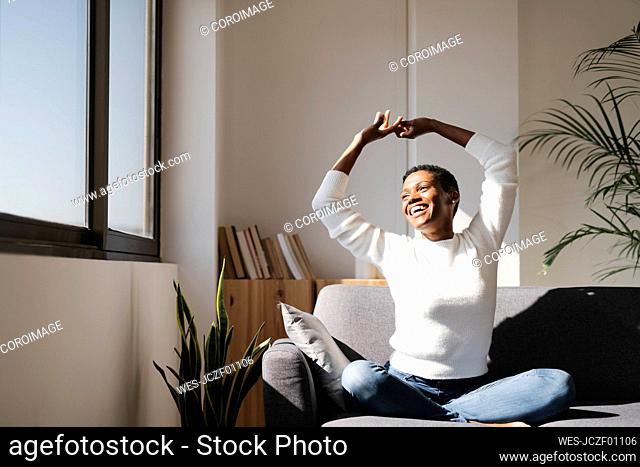 Laughing woman sitting on couch at home stretching her arms