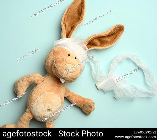 plush beige rabbit with a bandaged head with a white medical bandage on a blue background, top view