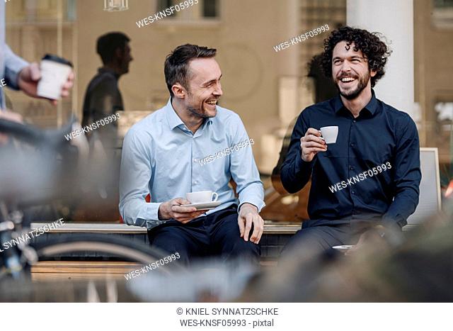 Friends sitting in front of coffee shop, talking, drinking coffee