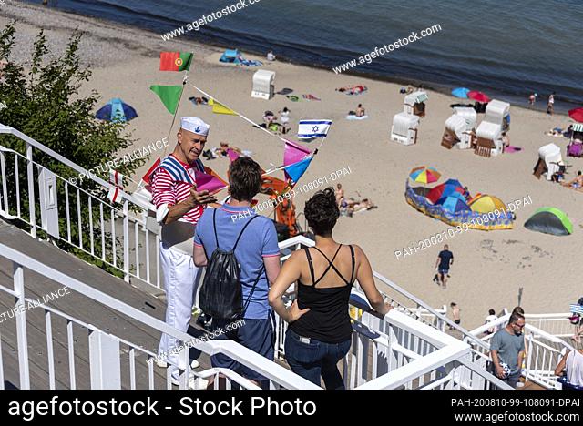 01 August 2020, Mecklenburg-Western Pomerania, Sellin: A ""sailor"" talks to holidaymakers at the pier. Sunny summer weather lures the holidaymakers to the pier