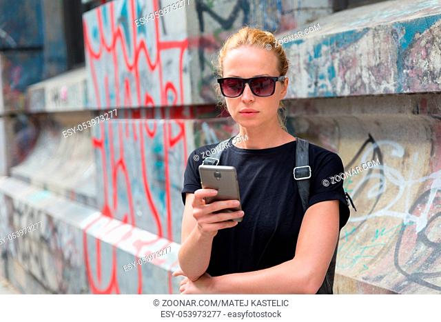 Closeup of female hipster with smart phone. Woman using smartphones against colorful graffiti wall in East Village, New York city, USA