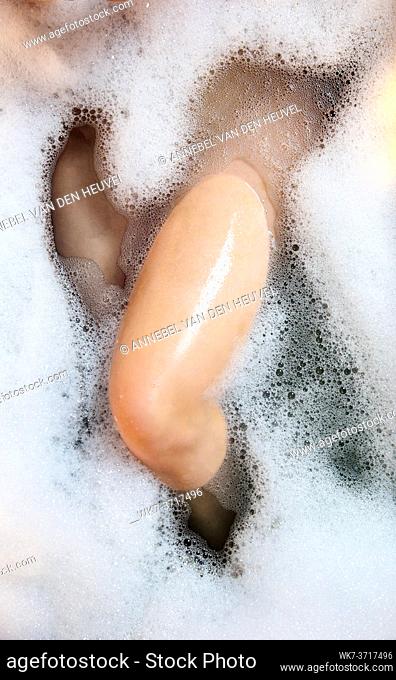 Women's legs in the bathtub, bathing with bubble bath foam top view, relaxtion beauty spa concept close up