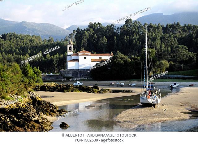View of the Ria de Niembro. A boat stranded at low tide in front of the church with the Sierra del Cuera the background. Llanes, Asturias, Spain