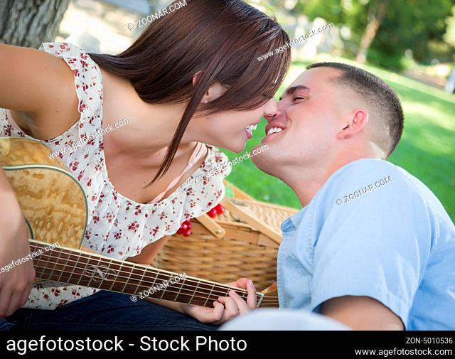 Affectionate Mixed Race Couple with Guitar Kissing in the Park
