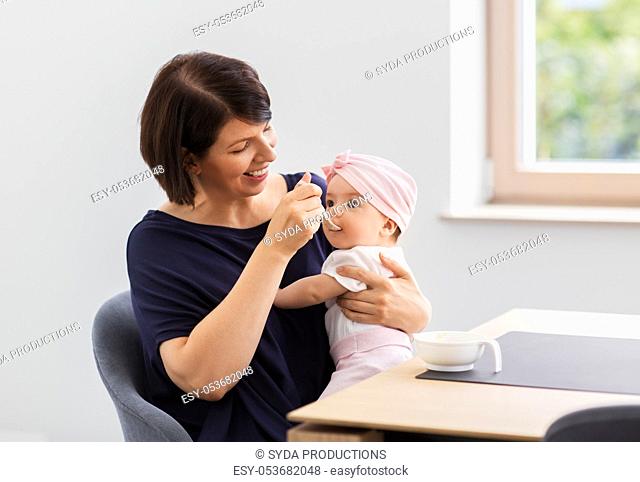middle-aged mother feeding baby daughter at home